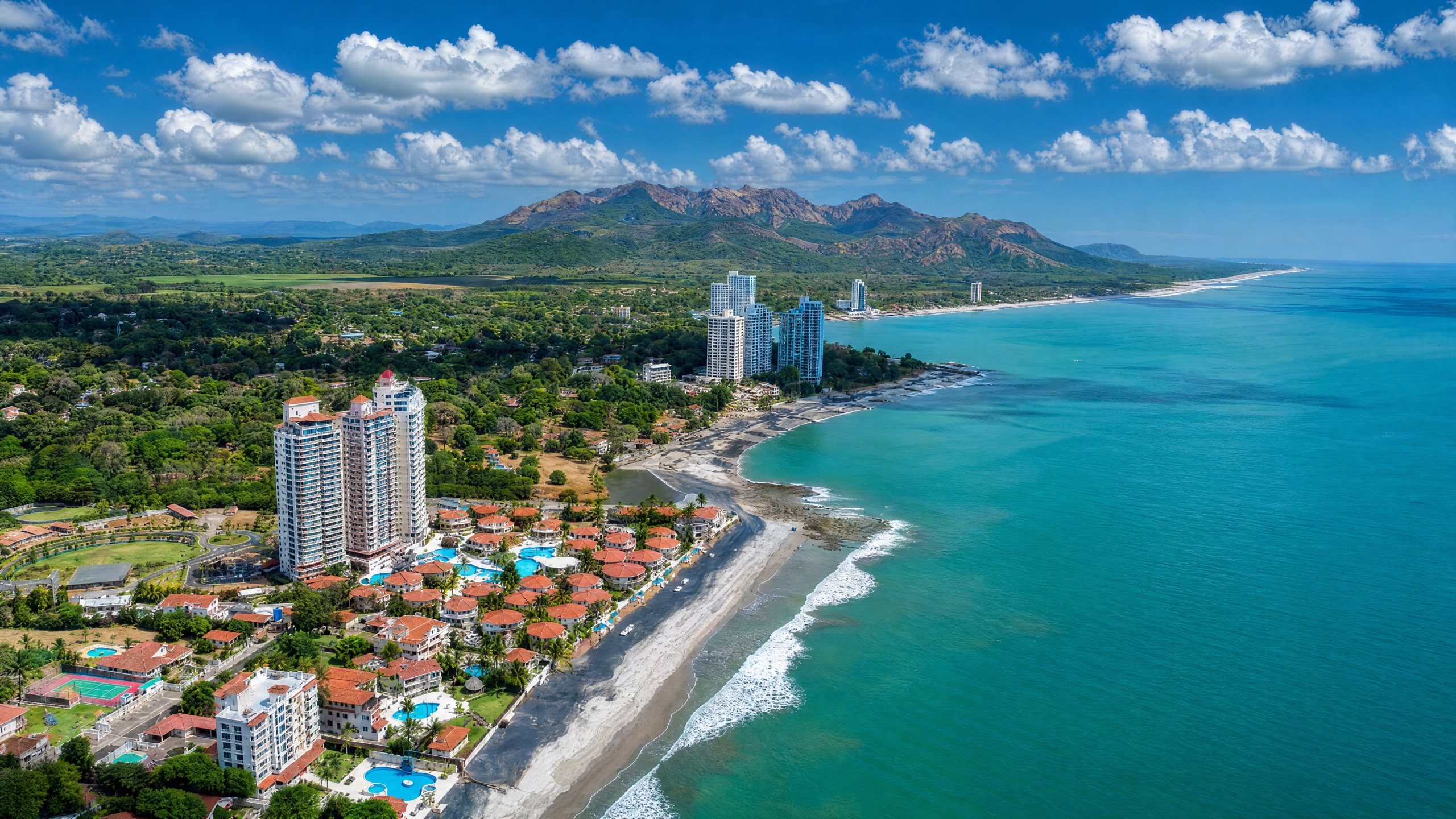 Aerial view of the Coronado and Playa Caracol beach corridor on the Pacific coast of Panama, low-rise modern beach villas and resort condos, palm trees and tan-sand beach meeting calm ocean.